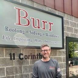 Employee standing in front of Burr Roofing Siding Windows business storefront sign at 11 Corinth address